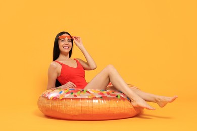 Happy young woman with beautiful suntan and sunglasses on inflatable ring against orange background