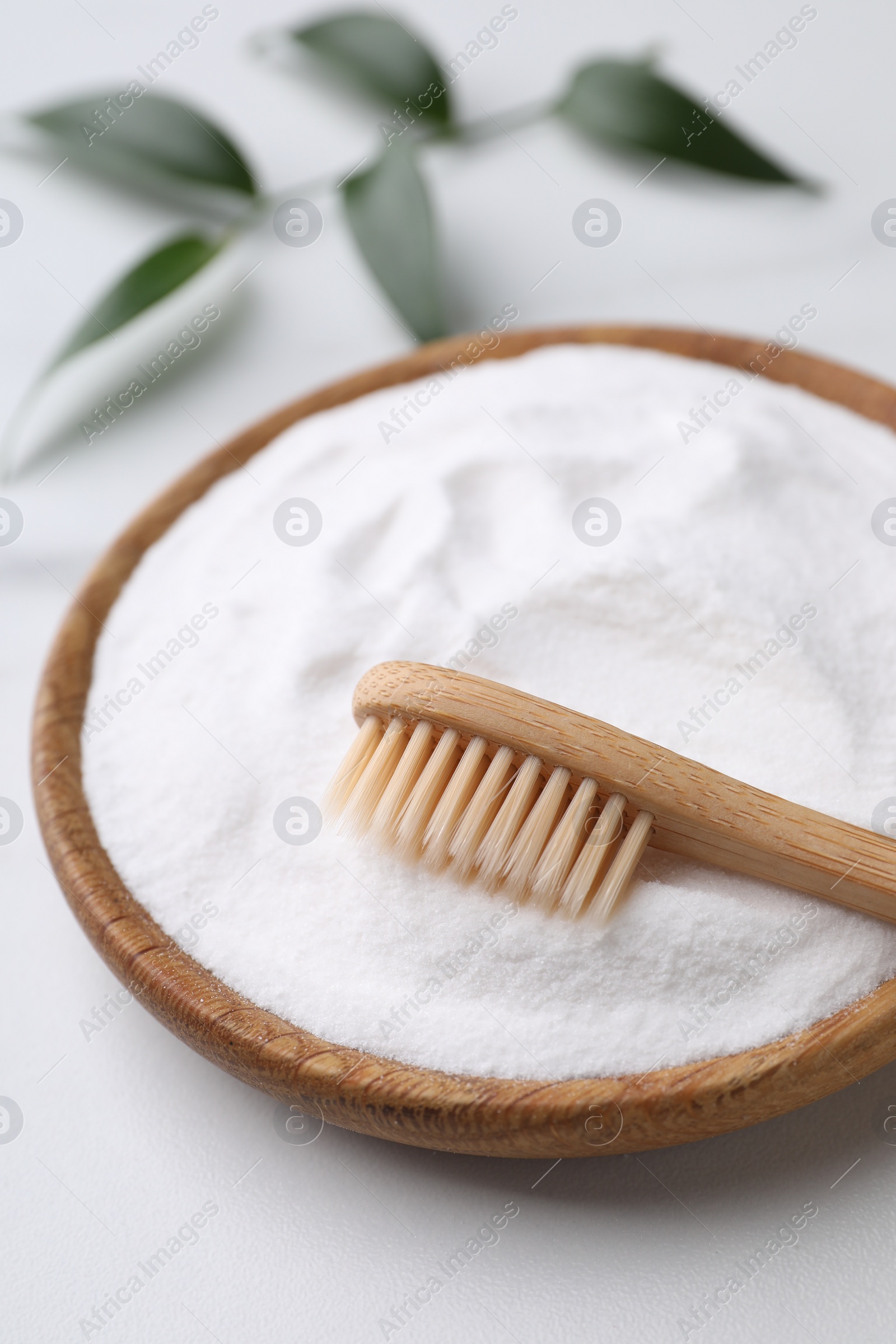 Photo of Bamboo toothbrush, green leaf and bowl of baking soda on white marble table, closeup