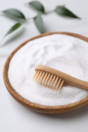 Photo of Bamboo toothbrush, green leaf and bowl of baking soda on white marble table, closeup