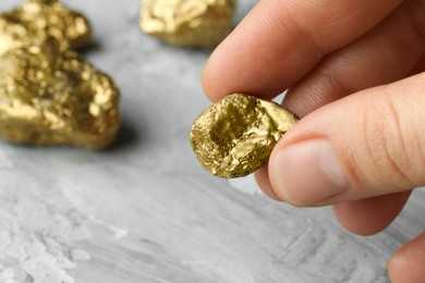 Woman holding gold nugget at grey textured table, closeup. Space for text