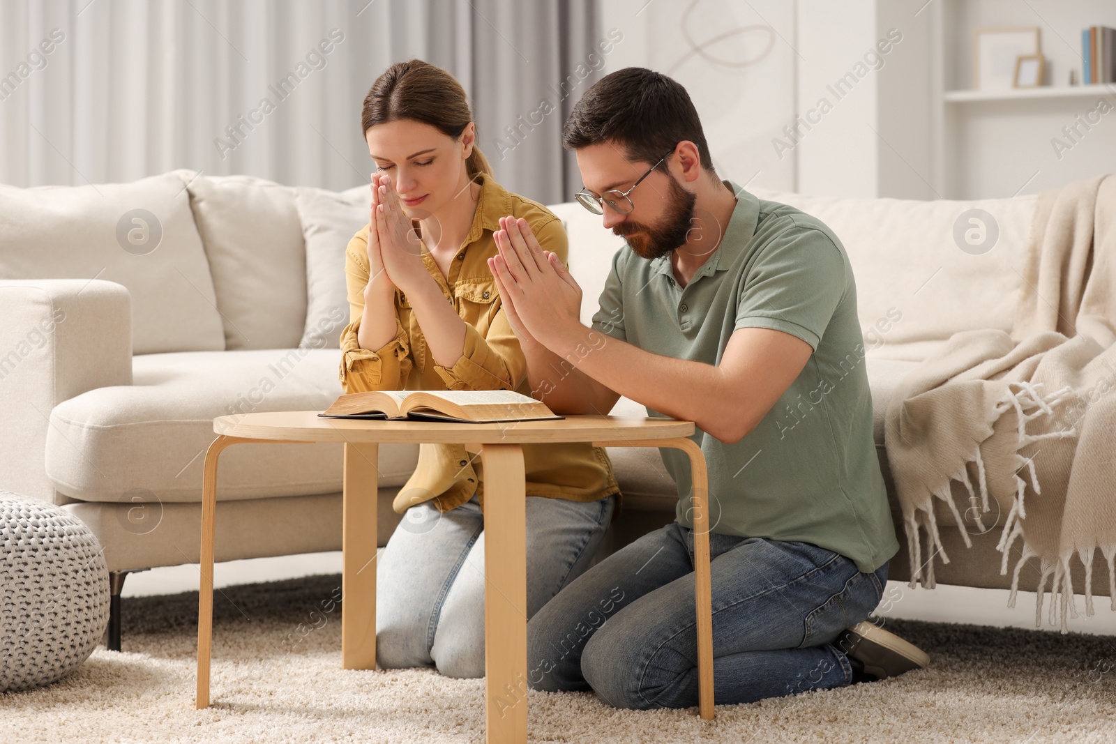 Photo of Family couple praying over Bible together at table indoors