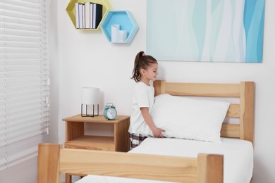Cute girl changing bed linens in children room