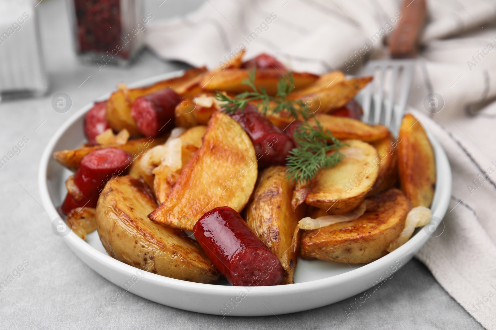 Photo of Delicious baked potato with thin dry smoked sausages, onion and dill on gray table, closeup