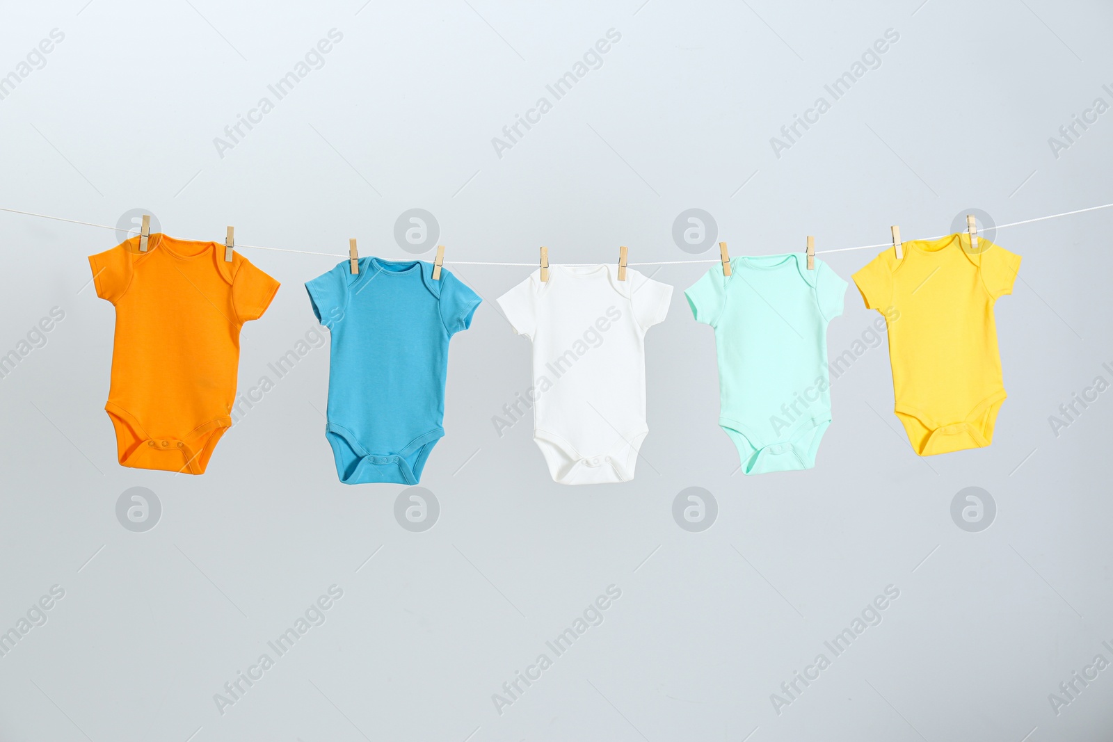 Photo of Different baby onesies hanging on clothes line against light grey background. Laundry day