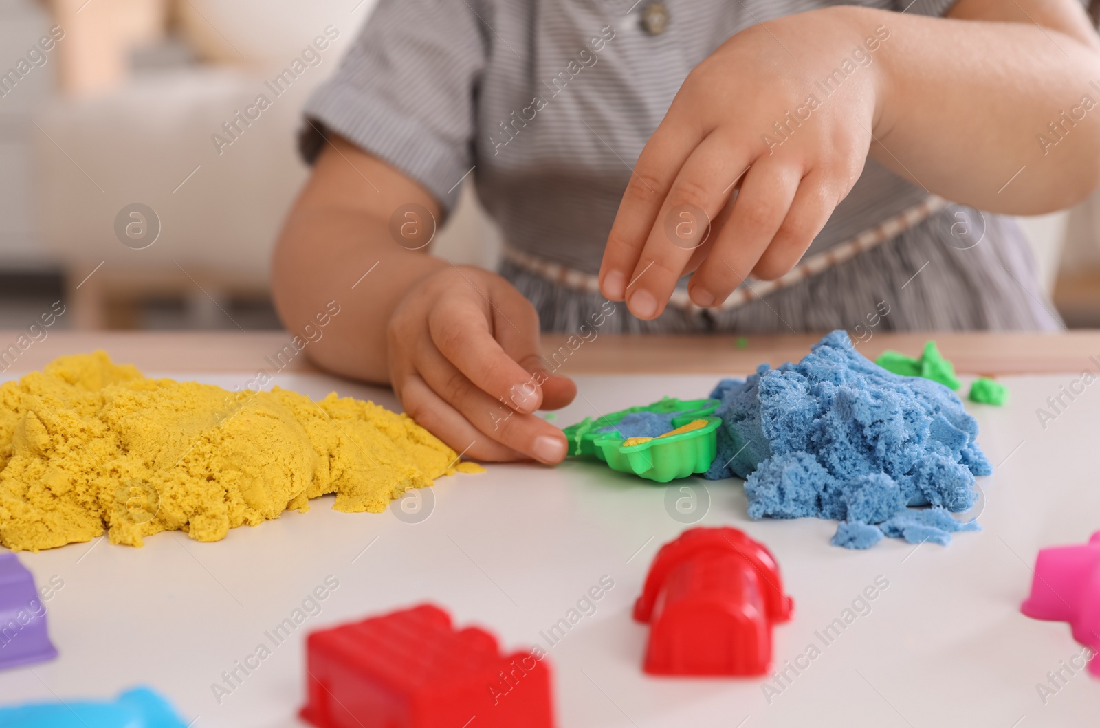 Photo of Little girl playing with bright kinetic sand at table indoors, closeup