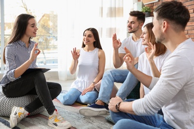 Group of young people learning sign language with teacher indoors