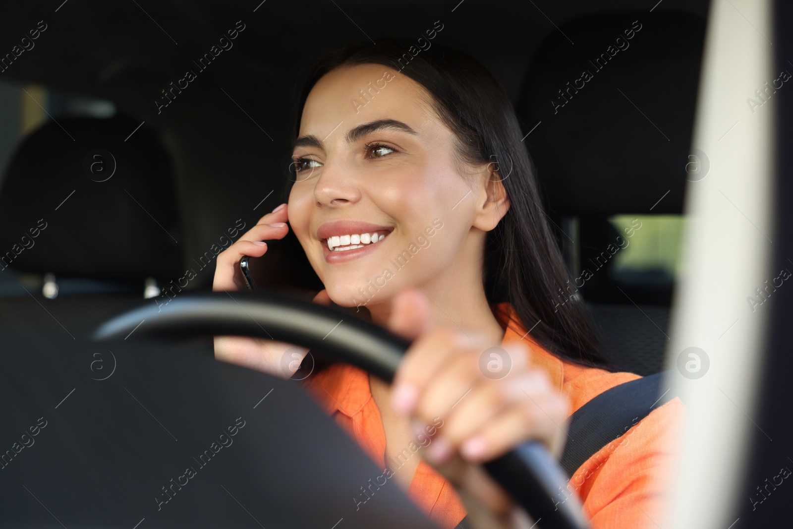 Photo of Happy young woman talking on smartphone in modern car, view through windshield