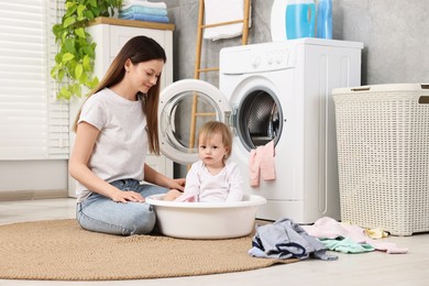 Mother with her daughter washing baby clothes in bathroom