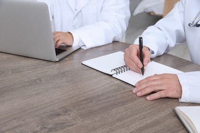 Doctors working at wooden table in clinic, closeup