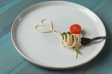 Photo of Heart made of tasty spaghetti, fork and tomato on light blue wooden table