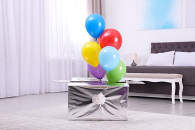 Photo of Gift box with bright air balloons in modern bedroom