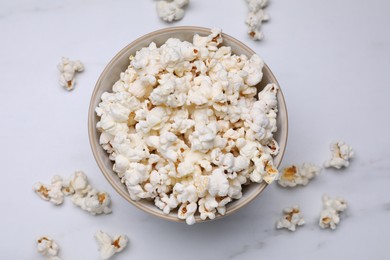 Photo of Bowl of tasty popcorn on white marble table, flat lay