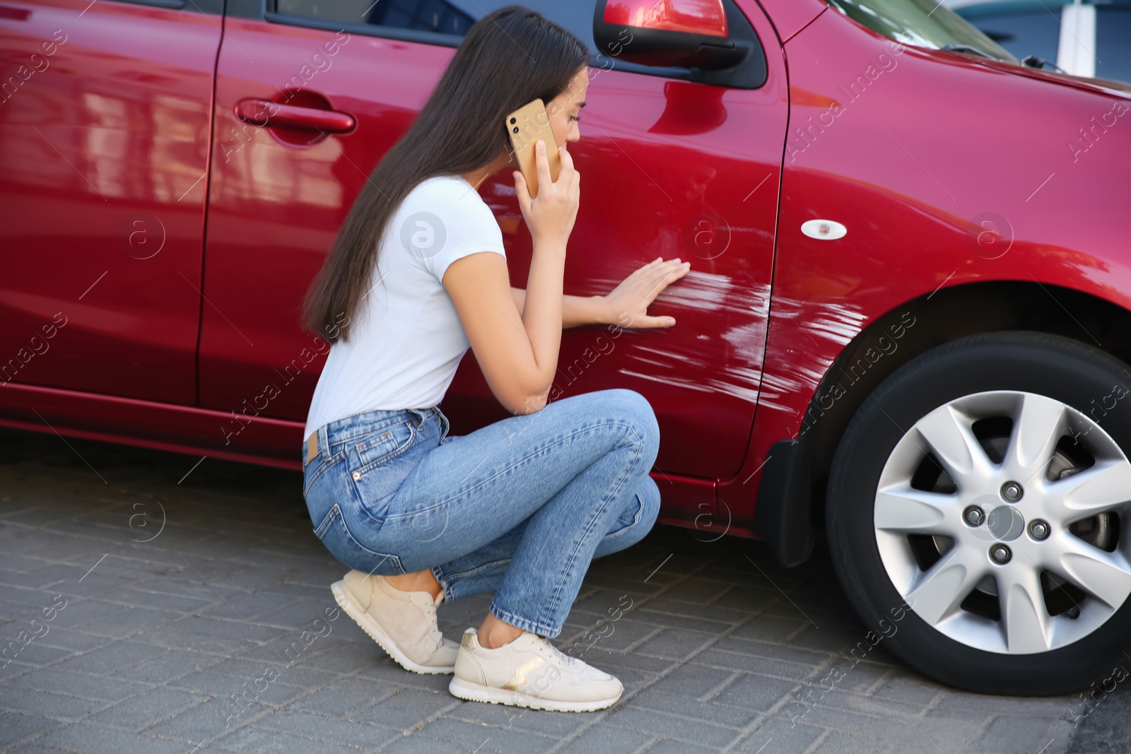 Photo of Stressed woman talking on phone near car with scratch outdoors