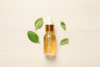 Photo of Bottle of essential basil oil and fresh leaves on white wooden table, flat lay