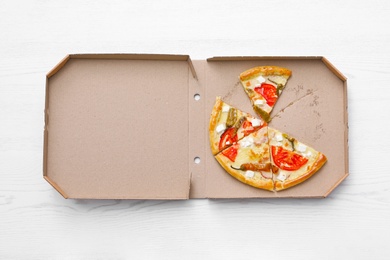 Cardboard box with tasty pizza slices on wooden background, top view
