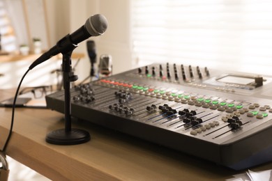 Photo of Microphone and professional mixing console on wooden table in radio studio