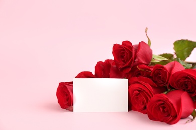 Photo of Beautiful red roses and blank card on pink background, space for text. St. Valentine's day celebration