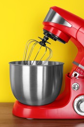 Photo of Modern red stand mixer on wooden table against yellow background