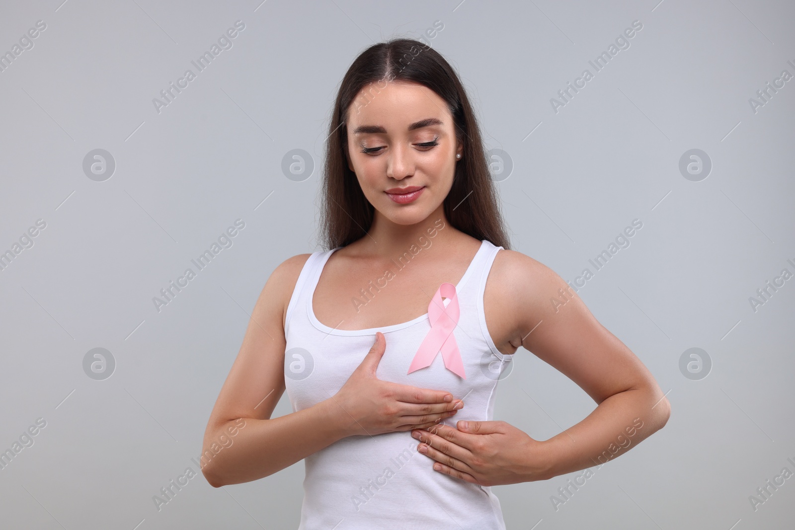 Photo of Beautiful young woman with pink ribbon on light grey background. Breast cancer awareness