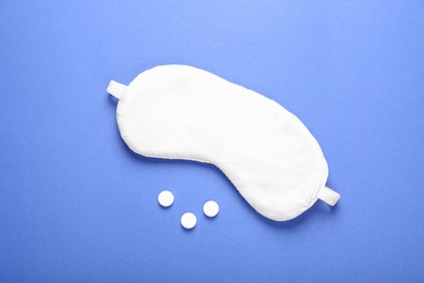 Photo of Soft sleep mask and pills on blue background, flat lay