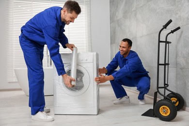 Photo of Male movers with stretch film wrapping washing machine in bathroom. New house