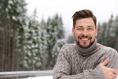 Man in warm sweater outdoors on snowy day, space for text. Winter vacation