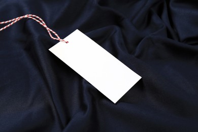 Photo of Blank white tag on dark blue fabric. Space for text