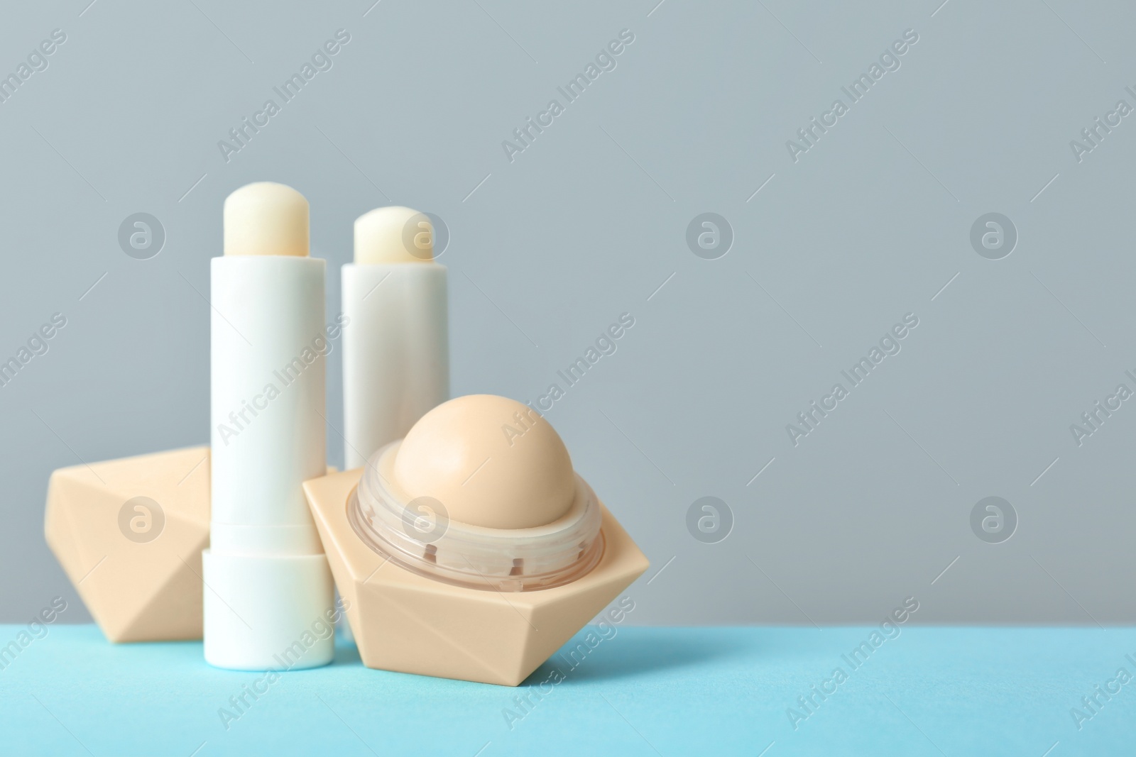 Photo of Hygienic lipsticks and balms on table against grey background