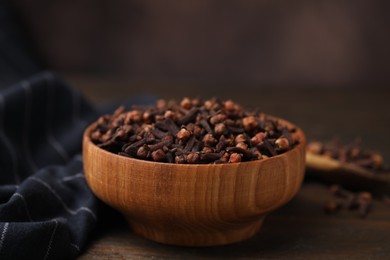 Photo of Aromatic cloves in bowl on wooden table against brown background, closeup