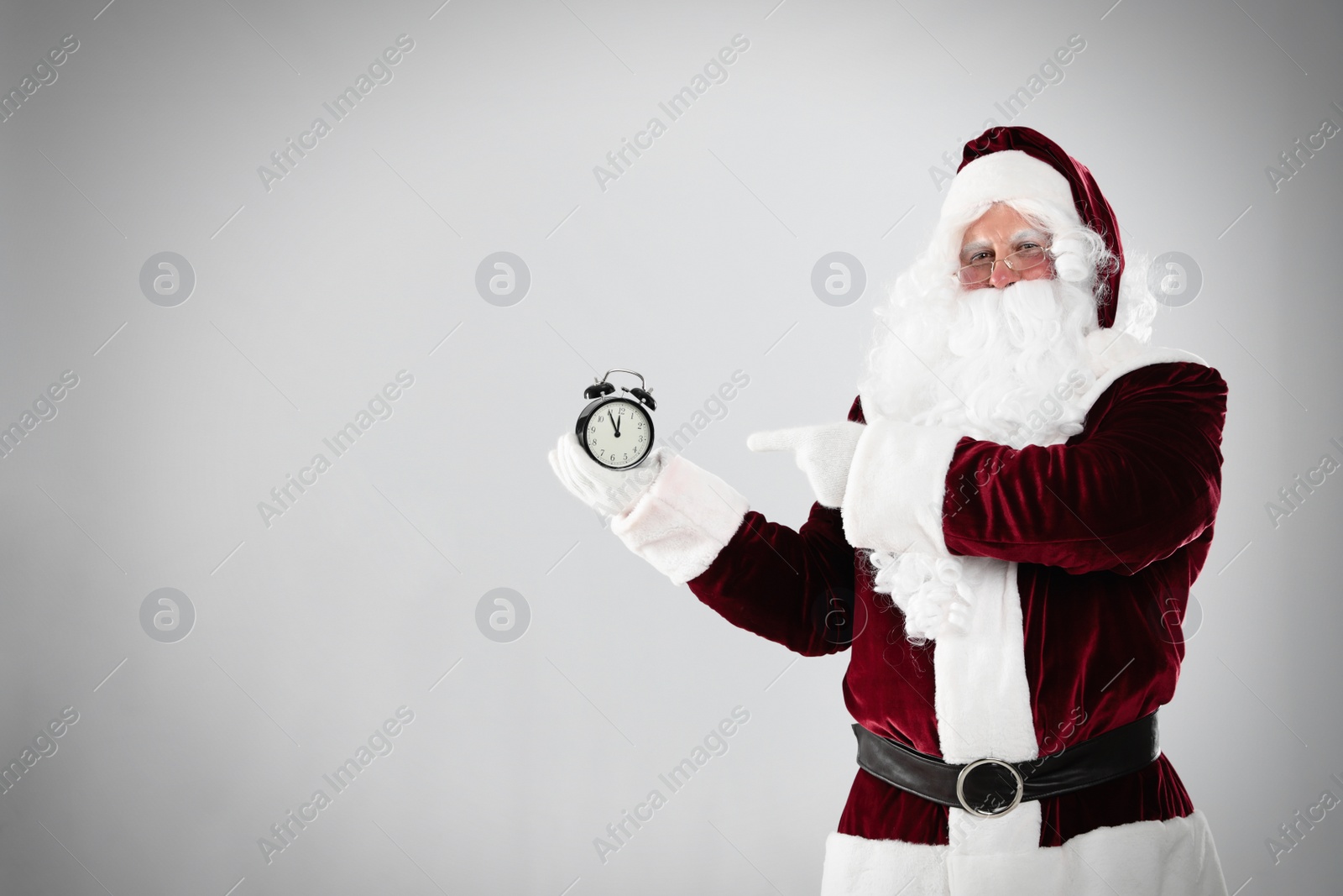 Photo of Santa Claus holding alarm clock on light grey background, space for text. Christmas countdown