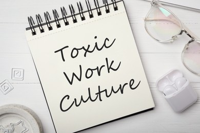 Notebook with text Toxic Work Culture on white wooden table, flat lay