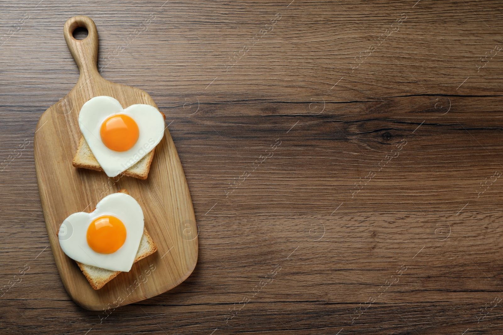 Photo of Heart shaped fried eggs and toasts on wooden table, top view. Space for text