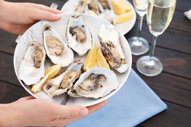 Photo of Woman with plate of fresh oysters over table, focus on hands