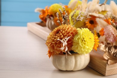 Small pumpkin with autumn bouquet on light wooden table, closeup. Space for text