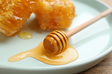 Photo of Tasty honey and wooden dipper on light blue plate, closeup