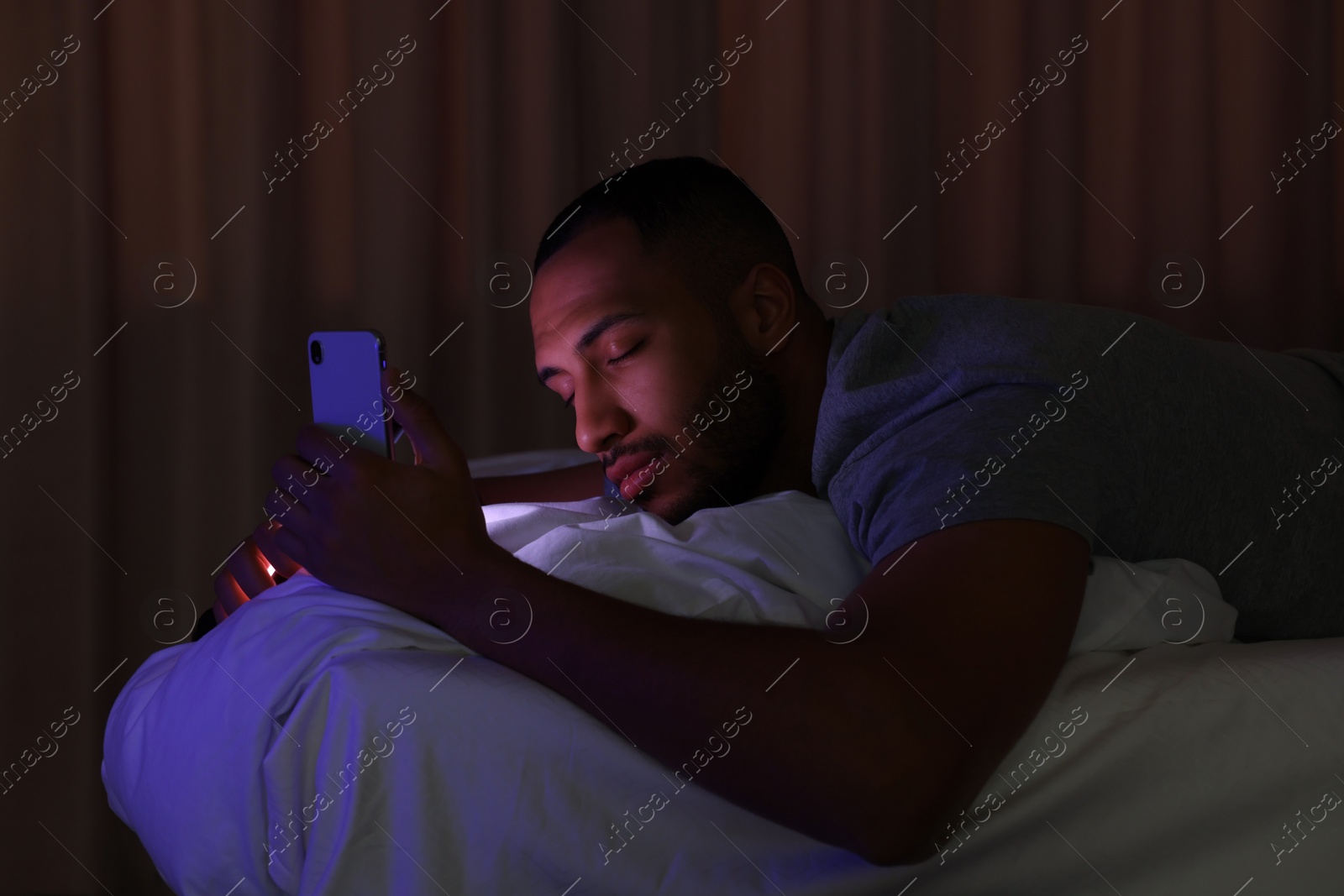 Photo of Young man sleeping while holding smartphone in bed at night. Internet addiction