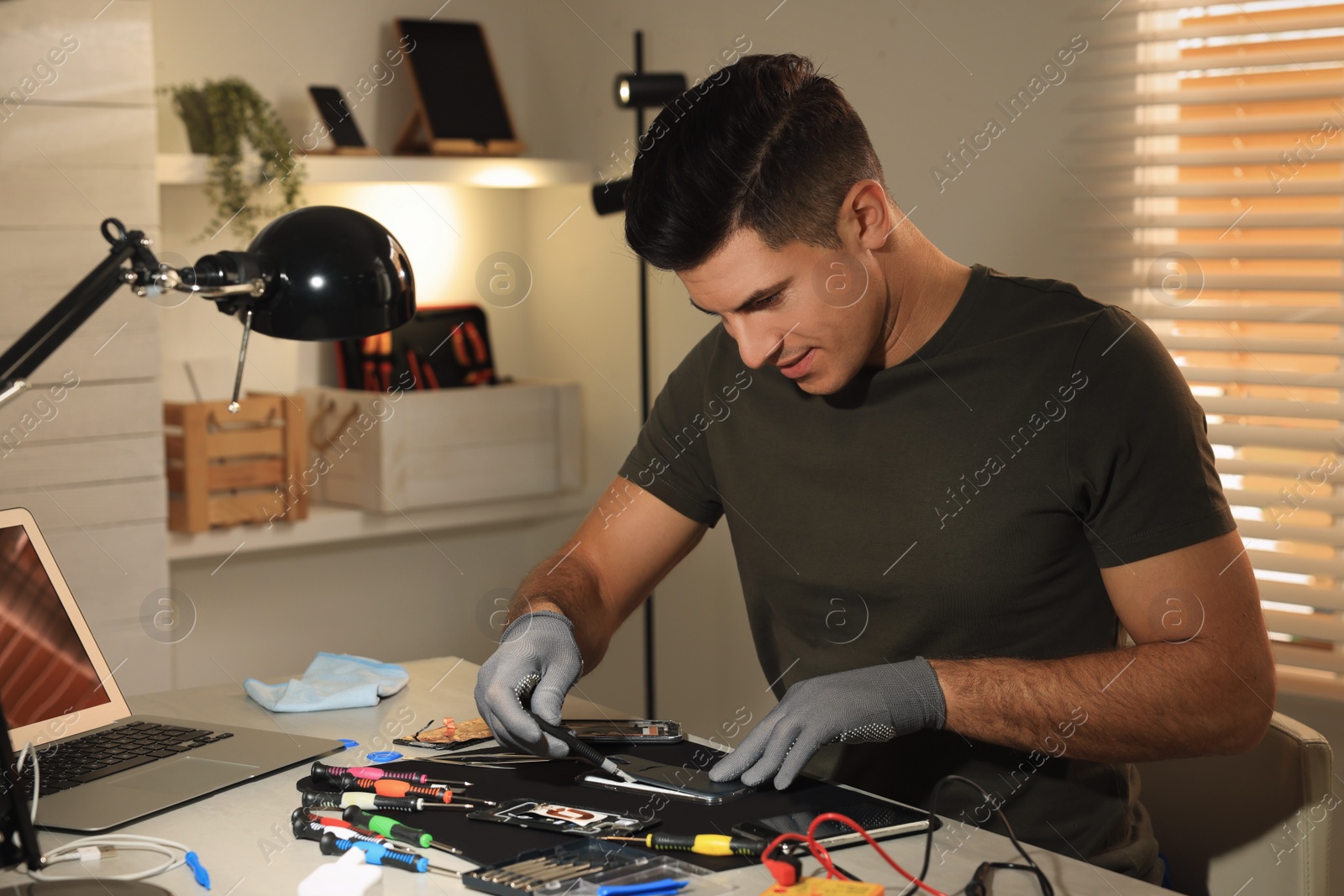 Photo of Technician repairing broken smartphone at table indoors