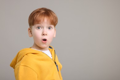 Portrait of surprised little boy on grey background, space for text