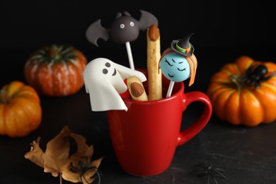 Photo of Different cake pops in cup decorated as monsters on black table. Halloween treat