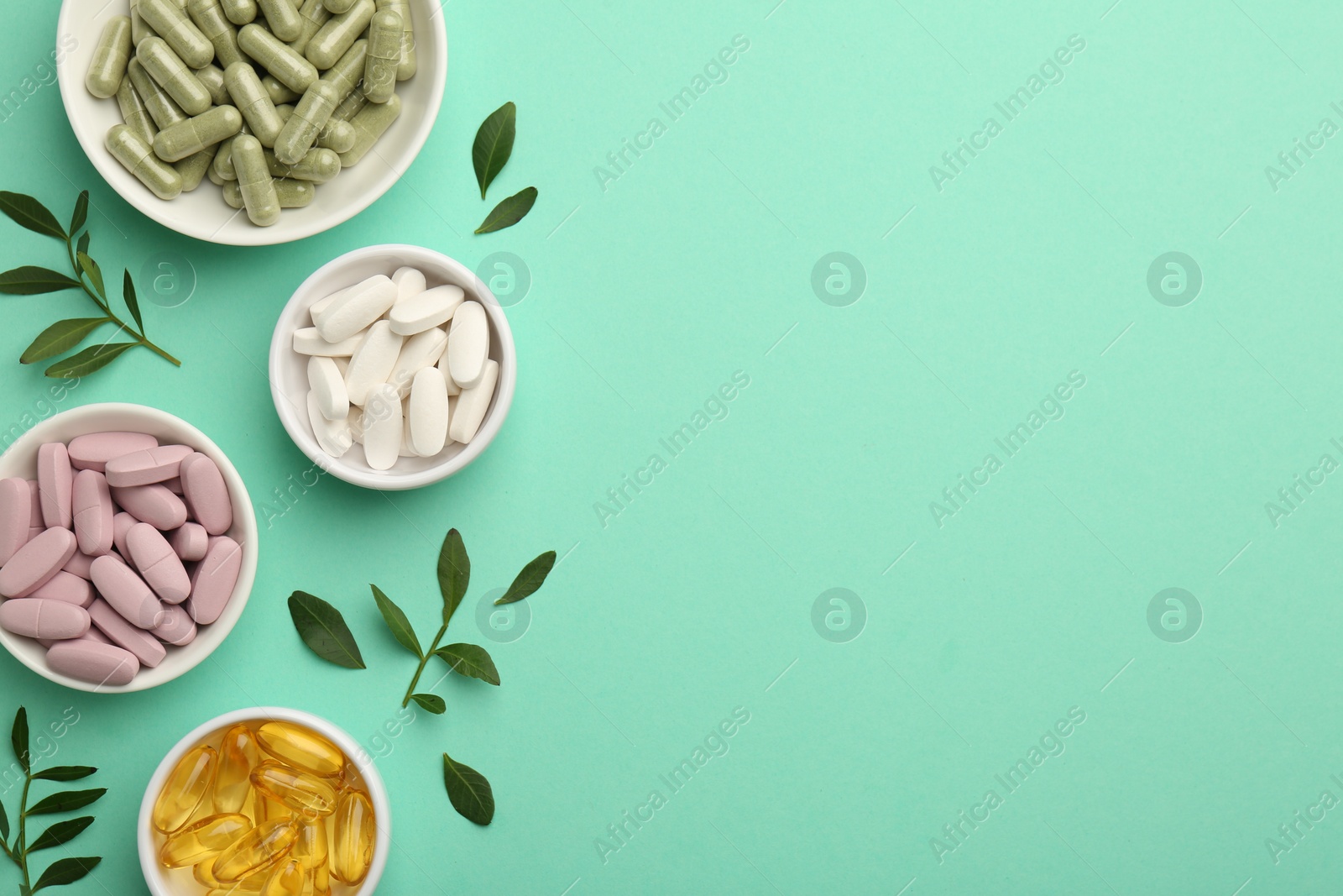 Photo of Different vitamin capsules in bowls and leaves on turquoise background, flat lay. Space for text