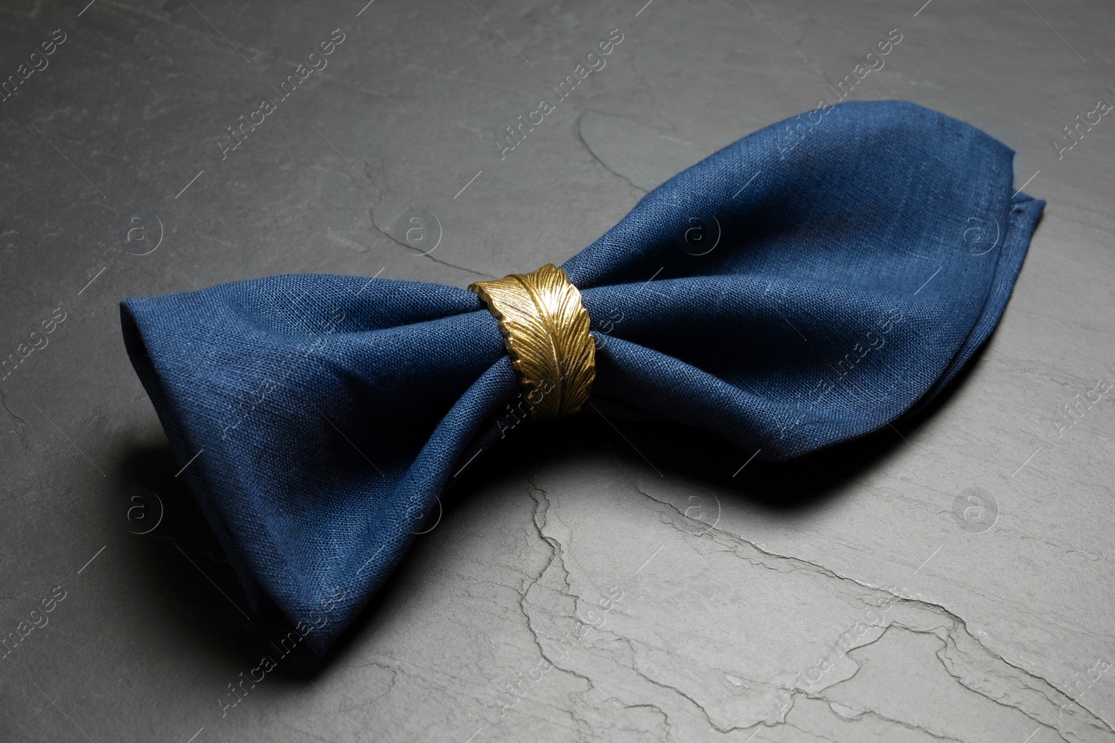 Photo of Blue fabric napkin with beautiful decorative ring on dark table