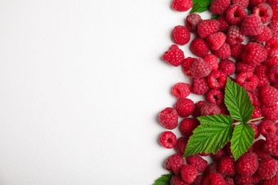 Photo of Fresh ripe raspberries with green leaves on white background, flat lay. Space for text