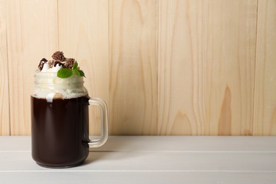 Photo of Mason jar of delicious hot chocolate with whipped cream and mint on white wooden table. Space for text