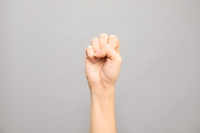 Woman showing S letter on grey background, closeup. Sign language