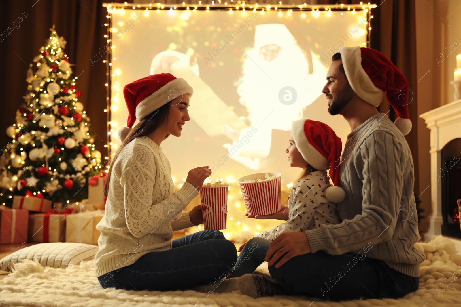 Photo of Family watching movie on projection screen in room decorated for Christmas. Home TV equipment