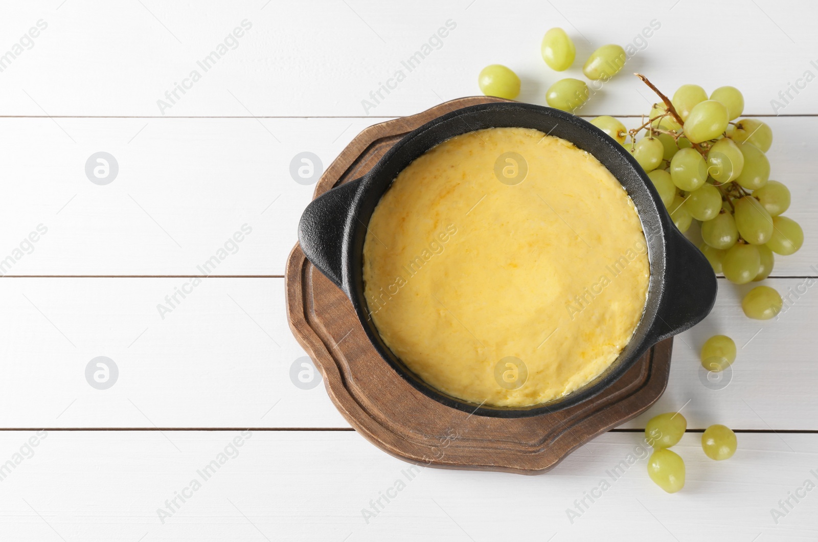 Photo of Fondue with tasty melted cheese and grapes on white wooden table, flat lay. Space for text