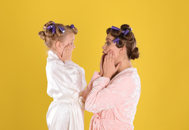 Photo of Emotional mother and daughter with curlers on yellow background