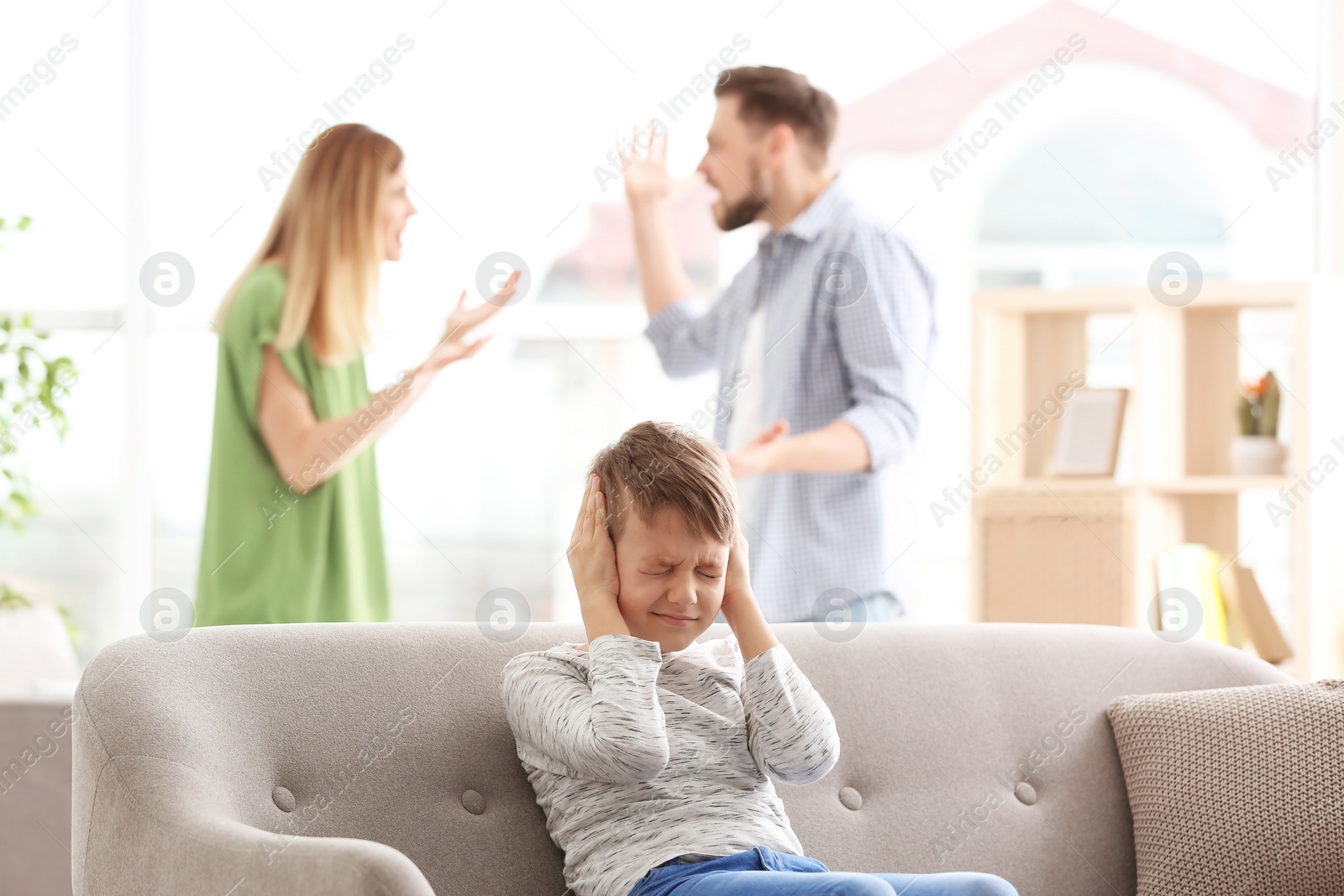 Photo of Little unhappy boy sitting on sofa while parents arguing at home