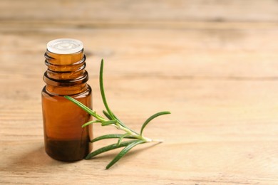 Bottle with essential oil and fresh rosemary on wooden table, space for text