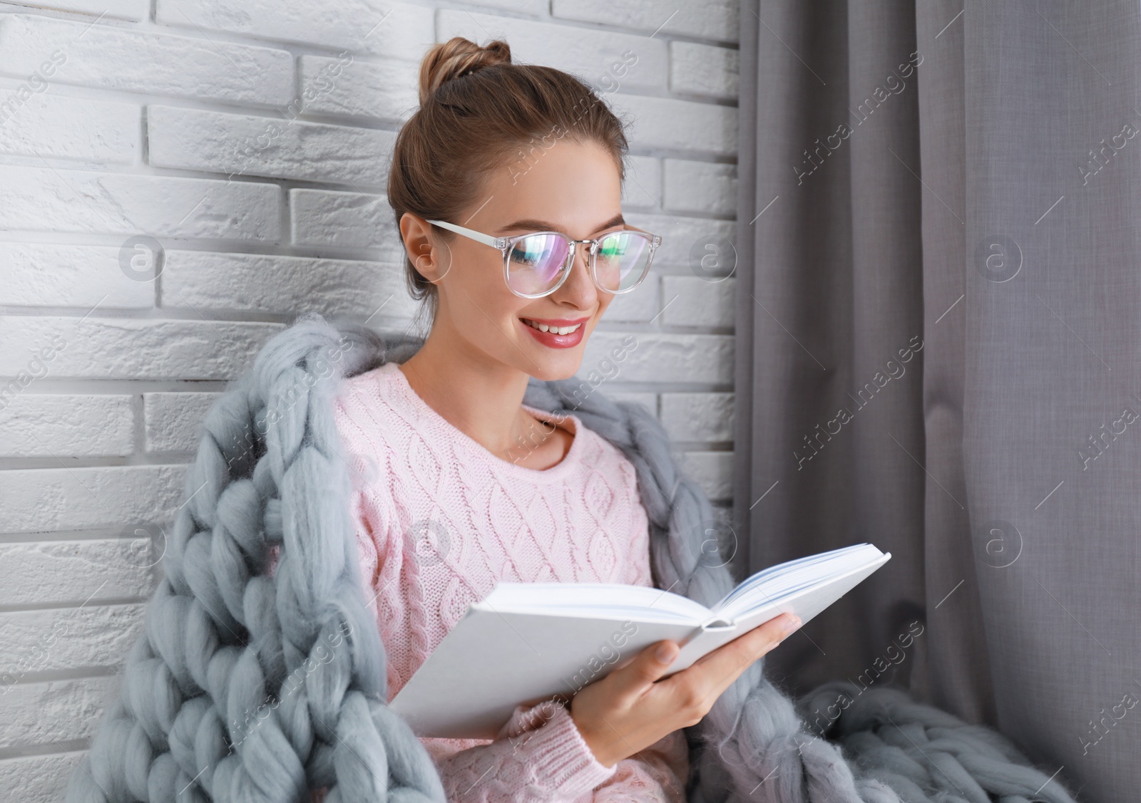 Photo of Young woman wearing knitted sweater with book at home